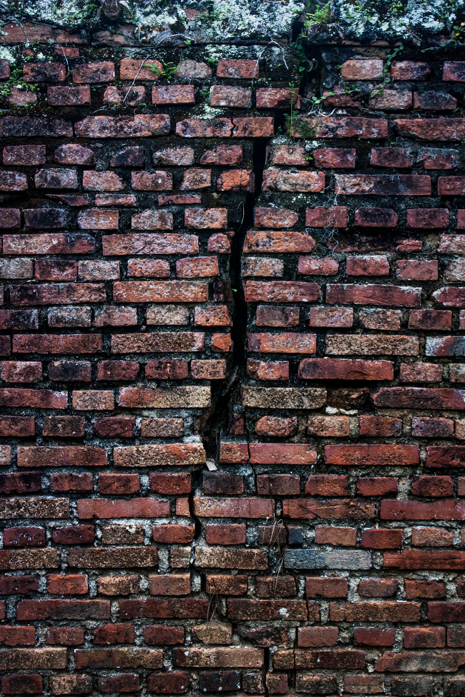 Grieta vertical partiendo los ladrillos de un muro antiguo, siguiendo las juntas de mortero