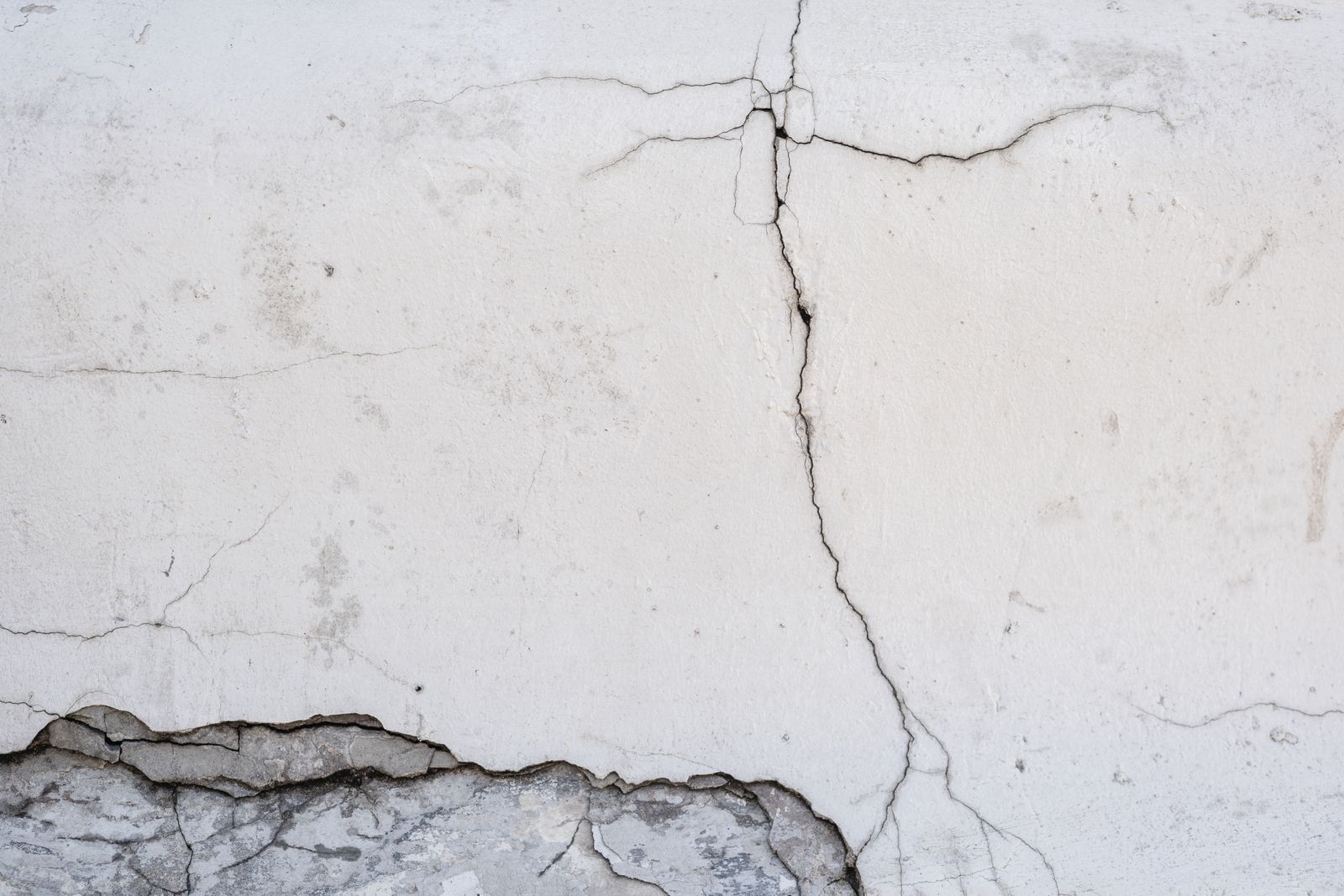 Grieta horizontal en la parte alta de una pared encontrándose con una grieta vertical que baja hasta una zona de revoco desprendido